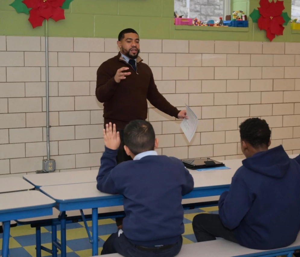 Anthony Morris speaking with students in a school classroom while a student raises a hand